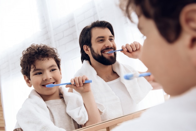 O pai e o filho escovam os dentes com escova de dentes.