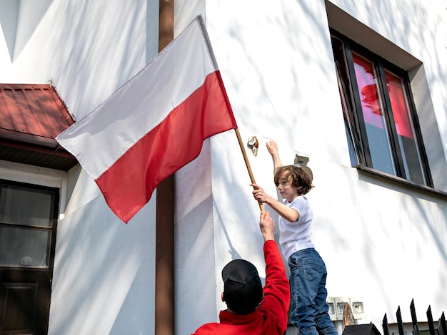 O pai e o filho estão pendurando uma bandeira polonesa no dia nacional polonês de 3 de maio