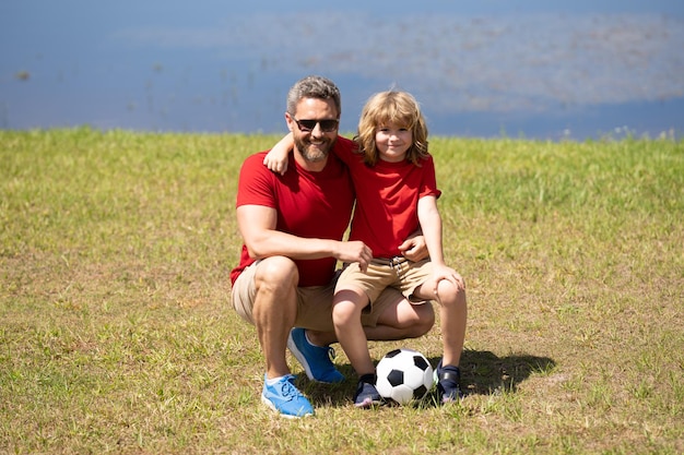 O pai e o seu filhozinho estão a divertir-se e a jogar futebol no gramado verde do verão.