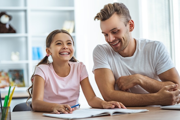 O pai feliz e uma filha fazendo lição de casa na mesa