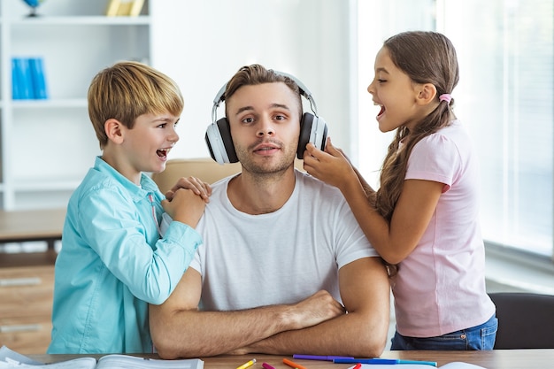 O pai feliz em fones de ouvido sentado com um menino e uma menina na mesa