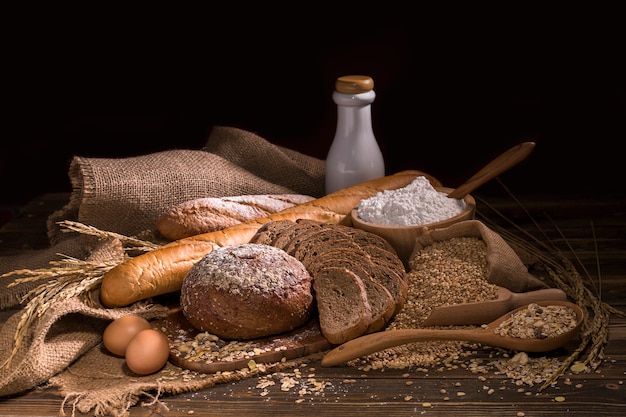 O pão integral inteiro, o leite, a farinha e o pano ensacam na tabela de madeira.