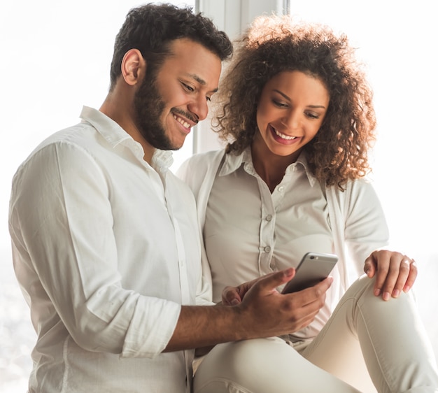 O par afro-americano bonito está usando um smartphone.