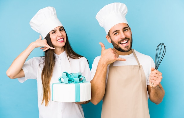 O par novo que cozinha um bolo junto isolou mostrar um gesto de chamada de telefone móvel com dedos.