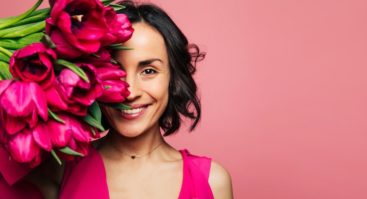 Foto o paraíso das meninas. retrato de uma linda menina morena em um vestido rosa e colar de ouro, que está olhando para a câmera, cobrindo uma parte do rosto com tulipas.