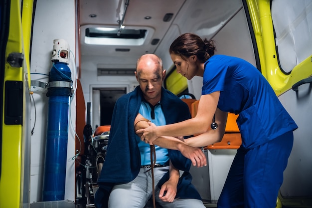 Foto o paramédico envolve um torniquete na mão de um homem ferido em uma ambulância.