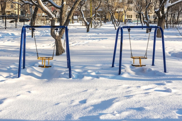 O parque infantil com baloiços está coberto de neve após uma queda de neve Paisagem da cidade de inverno