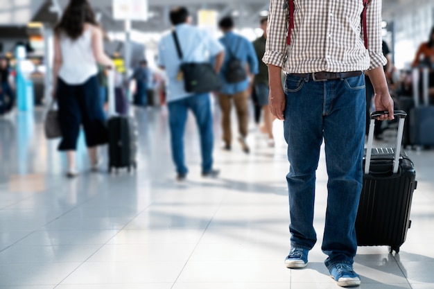 O passageiro com cartão de embarque no saco de trás e mala rolante na estação de transporte.