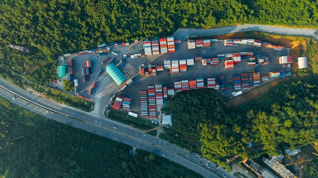 O pátio de contêineres de carga ao lado da estrada e cercado por empilhadeiras de montanhas e carga no depósito