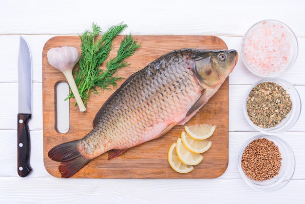 O peixe fresco da carpa encontra-se em uma placa de corte com vista superior das especiarias e dos temperos