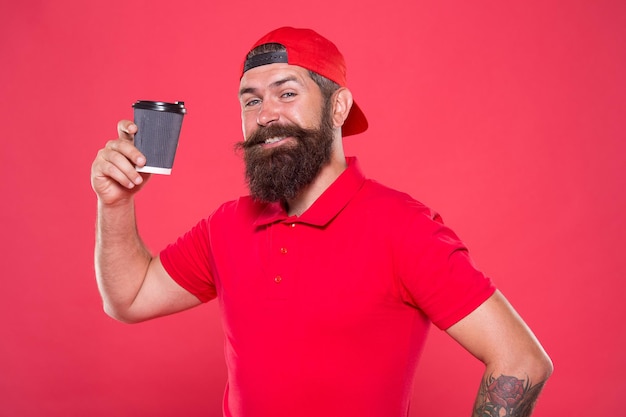 O pessoal da cafeteria queria. Barista preparou bebida para você. Barista alegre. Homem barbudo hipster boné vermelho uniforme segurar a xícara de café de papel. Barista recomenda bebida com cafeína. Cargo de barista.