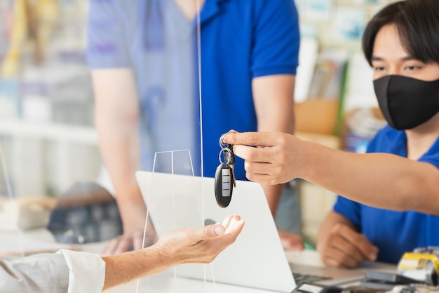 O pessoal da recepção devolve a chave do carro ao cliente. Jovem que trabalha no centro de serviço de carro de garagem usando máscara facial para cuidados de saúde.