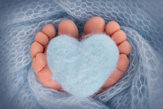 O pezinho de um bebê recém-nascido pés macios de um recém-nascido em um cobertor azul claro close-up dos calcanhares e pés de um recém-nascido coração azul de malha nas pernas de um bebê fotografia macro de estúdio