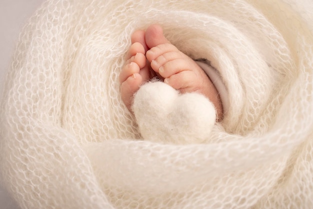 O pezinho de um bebê recém-nascido pés macios de um recém-nascido em um cobertor de lã branca close-up dos calcanhares e pés de um recém-nascido coração branco de malha nas pernas de um bebê macrofotografia