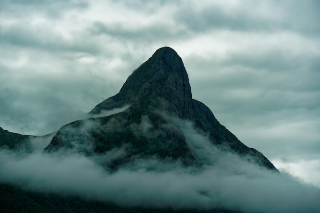 O pico da montanha rochosa nas nuvens. Noruega.
