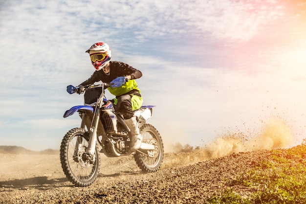 Foto o piloto profissional da motocicleta do motocross conduz através da fumaça e da névoa sobre a trilha da estrada de terra.