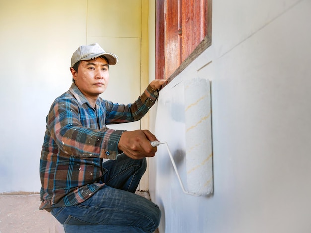 Foto o pintor dos trabalhadores está a pintar as paredes de madeira da sala de branco com a melhoria do rolo de pintura