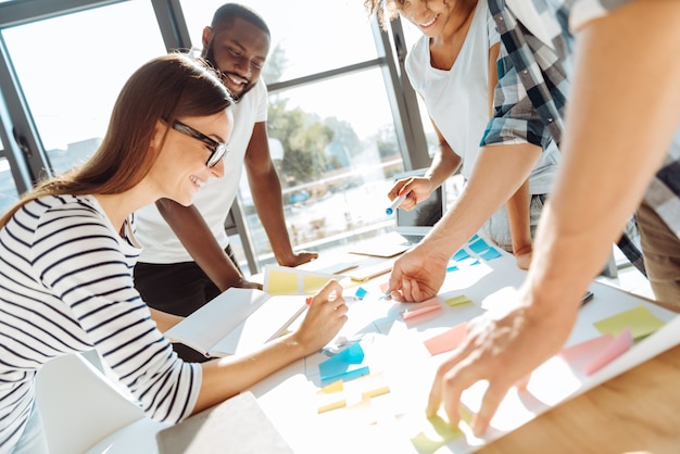 O planejamento é importante. Jovens colegas positivos trabalhando no escritório e usando post-its enquanto planejam seu trabalho
