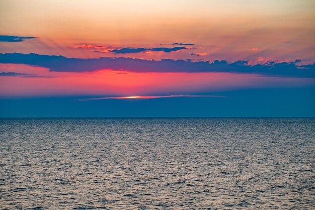 Foto o pôr-do-sol sobre a superfície da água do mar e os raios vermelhos do sol se espalhando