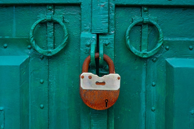 O portão de metal está trancado com cadeado. Cadeado enferrujado no portão, close-up. Portas de ferro bruto.