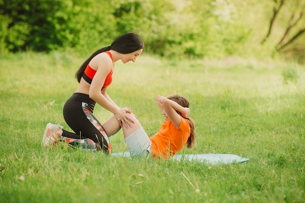 O preparador físico ajuda a garota a completar o exercício. Faça esportes ao ar livre.