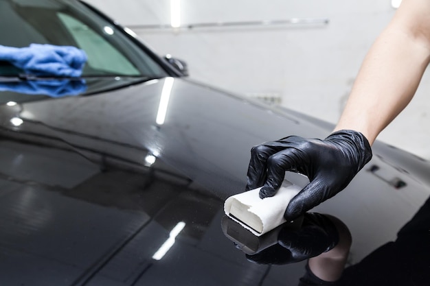 O processo de aplicação de um revestimento nanocerâmico no capô do carro por um trabalhador do sexo masculino com uma esponja e composição química especial para proteger a pintura da carroceria de arranhões, lascas e danos