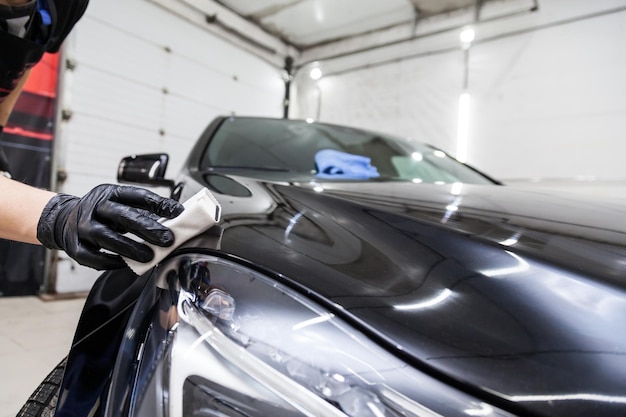 O processo de aplicação de um revestimento nanocerâmico no capô do carro por um trabalhador do sexo masculino com uma esponja e composição química especial para proteger a pintura da carroceria de arranhões, lascas e danos
