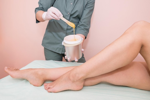 Foto o processo de depilação das pernas pelo método de shugaring usando pasta de glicoseremoção de pêlos de açúcar cosmetológico de pernas femininas em um centro de spa