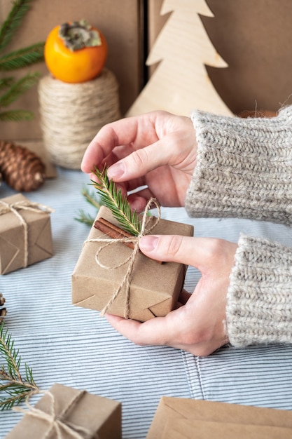 O processo de embalagem de presentes modernos e elegantes para o Natal e o Ano Novo. Caixas para presente em papel Kraft, barbante e galhos de árvores de Natal. Fundo de Natal, atmosfera de férias.