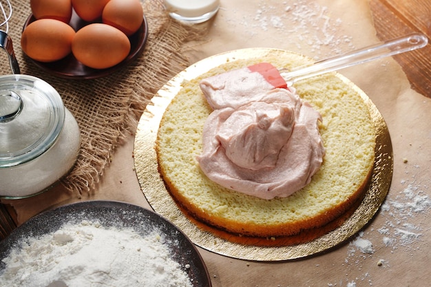 O processo de fazer bolo caseiro Creme de morango rosa espalhado sobre uma camada Biscoito de esponja para fazer em casa Foto de alta qualidade