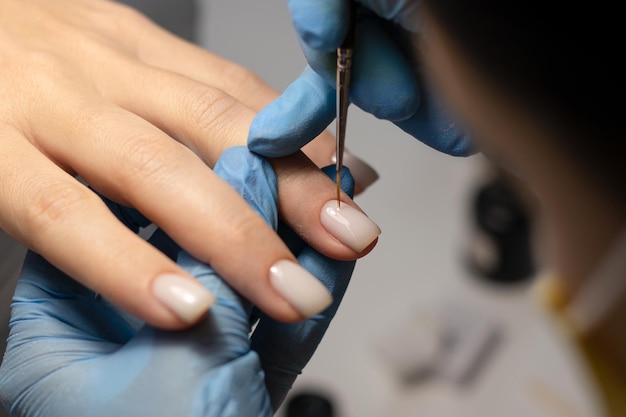 O processo de fazer uma manicure em um salão de spa. Manicure aplica esmalte de gel leitoso nas unhas