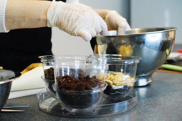 O processo de preparação de uma sobremesa multicamadas O confeiteiro apresenta camadas de caramelo e biscoito de nozes em um molde plástico Foto horizontal