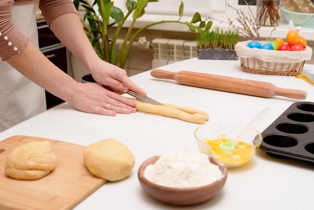 O processo de rolar a massa em casa sobre a mesa está nas mãos de uma mulher para fazer bolinhos festivos de cruffins para a páscoa