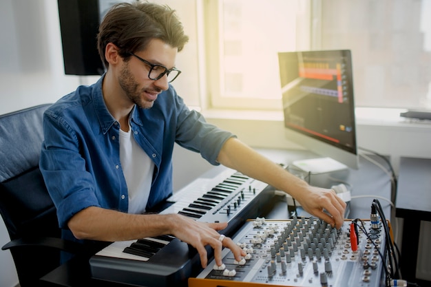 O produtor musical está compondo uma música no teclado sintetizador e no computador no estúdio de gravação. homem está trabalhando no mixer de som no estúdio de gravação ou dj está trabalhando no estúdio de transmissão