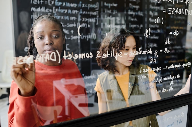 O professor a escrever códigos no quadro preto juntamente com o aluno na sala de aula
