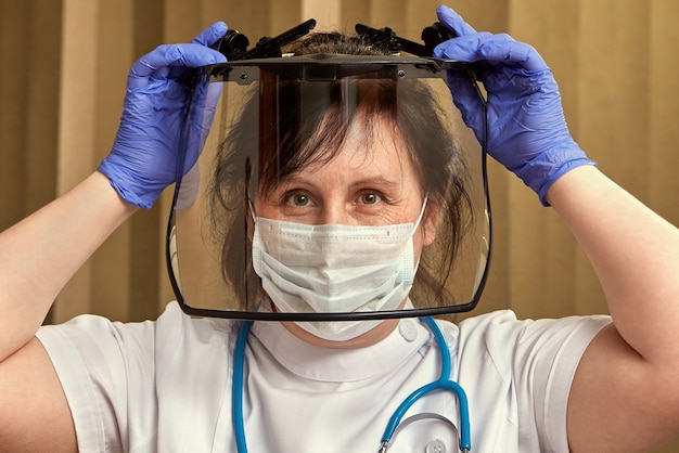 O profissional de saúde com máscara de proteção médica, luvas e óculos está colocando equipamento cirúrgico para se proteger durante a pandemia de coronavírus.