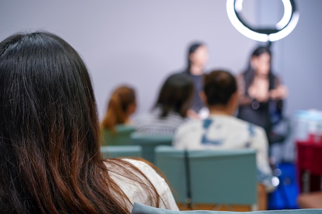 O público e o participante ouvem o professor e o palestrante na frente do palco sobre maquiagem facial feminina