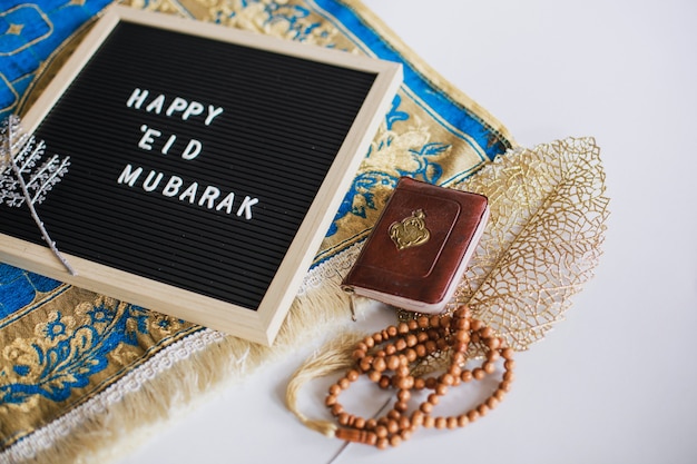 Foto o quadro diz: feliz eid mubarak no tapete de oração com o livro sagrado al quran e contas de oração. há uma letra árabe que significa o livro sagrado