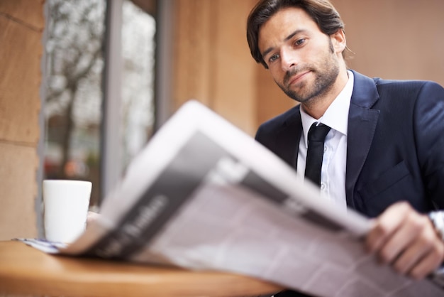 O que está acontecendo no mundo dos negócios hoje Um jovem empresário lendo um jornal ao ar livre em um café