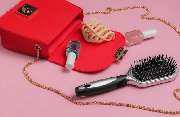 O que está na bolsa feminina Bolsa de couro vermelha com acessórios femininos, produtos cosméticos em fundo rosa