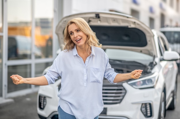 O que fazer. Mulher loira em pé no carro e parecendo indefesa