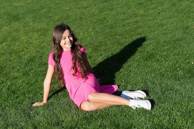 O que torna a criança feliz. Férias de verão. Ideias de férias. Menina feliz e sorridente desfrutar de relaxar no gramado. Aluna alegre. Divirta-se. Linda garota garoto sente-se grama verde. Criança feliz emocional relaxante ao ar livre.