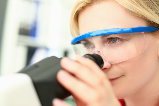 O químico fêmea nos vidros olha no microscópio