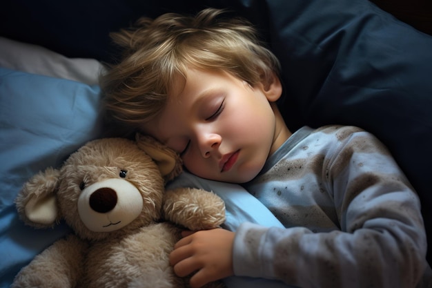 O rapaz dorme doce na cama com um urso de brinquedo nos braços debaixo do cobertor.