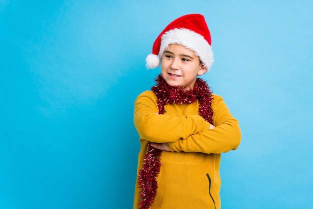 O rapaz pequeno que comemora o dia de Natal que veste um chapéu de Santa isolou o sorriso seguro com braços cruzados.