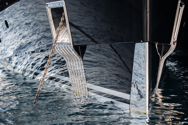 O reflexo hipnotizante da água no lado brilhante de um enorme iate ancorado, detalhes cromados, correntes e cordas descem para a água. Foto de alta qualidade