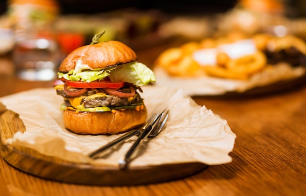 O restaurante tem um hambúrguer com molho de queijo de carne, tomate fresco e salada em um platô de madeira