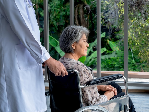O retrato aproximado de uma paciente idosa asiática feliz senta-se em uma cadeira de rodas enquanto o médico de jaleco branco cuida do consultório médico no hospital Cuidados de saúde e conceito médico