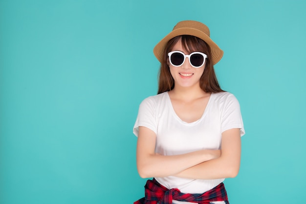 O retrato asiático novo do desgaste de mulher do retrato bonito e a expressão de sorriso dos óculos de sol seguros apreciam o verão nas férias isoladas no fundo azul.