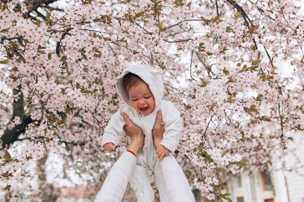 O retrato da criança alegre feliz na roupa branca sobre a árvore floresce o fundo da flor.